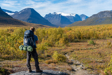 A hiker explores the autumn landscapes near Kebnekaise, Sweden's highest mountain, surrounded by vibrant fall colors. 