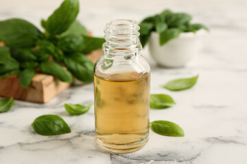 Glass bottle of basil essential oil and leaves on white  marble table