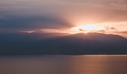 dramatic landscape with cinematic colors of sunrise rays light above mountains silhouette and sea, panoramic picturesque majestic view, fuzzy unfocused concept photo
