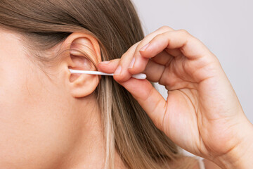 Obraz premium Cropped shot of a young caucasian woman cleaning her ear with a cotton swab isolated on a white background. Hygiene and health care. Close-up