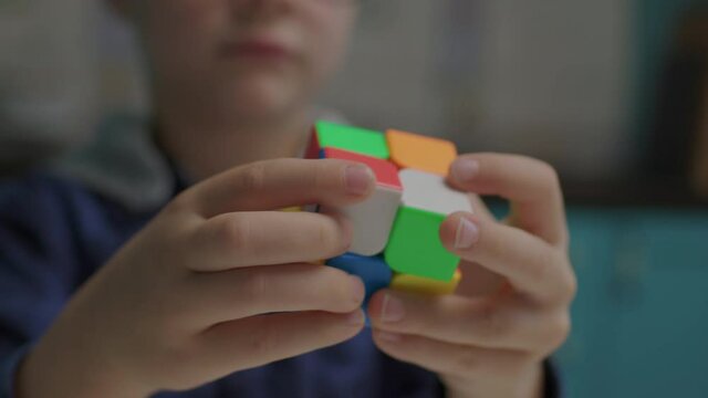 Close up of school boy in eye glasses solving color cube jigsaw in hands. Smart child playing with cube puzzle.