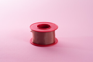 View of roll of medical or surgical tape for first aid on pink background. Silk tape.