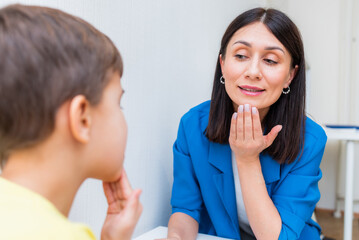 Woman speech therapist helps a boy correct the violation of his speech - obrazy, fototapety, plakaty