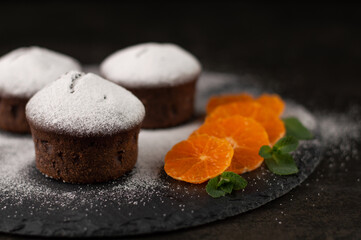 Blurred image of powdered sugar chocolate muffins on a dark background.