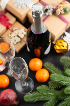 Blurred image of champagne and glasses, gifts, spruce twigs, tangerine on a dark background.
