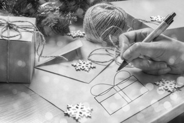 Female hand writing a Christmas letter for Santa, drawing a gift box on the table with an envelope,...