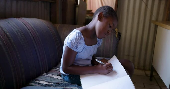 Poverty. Inequality. Young Black African girl doing schoolwork in a shack in a township