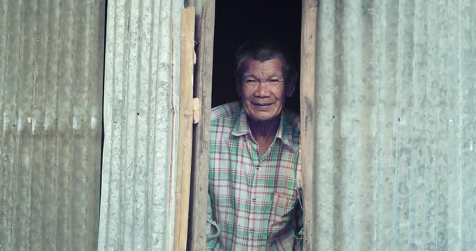 An Asian man who is more than seventy years old and works as a wage earner in a farm, live in a poor house. The lid and roof are galvanized sheet, opening the door smiling