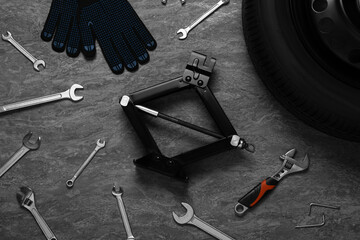 Car wheel, scissor jack, gloves and different tools on grey stone surface, flat lay