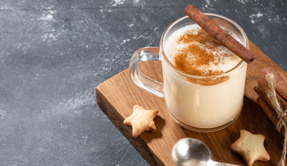 Glass mug with Christmas drink eggnog and heart shape cookies on wooden kitchen board on grey.