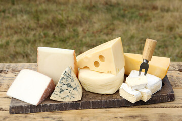 Different types of delicious cheeses on wooden table outdoors