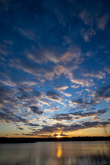 a beautiful blue lake with some tree silhouettes in the foreground under a dramatic sunset sky. High quality photo