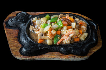 A traditional Japanese dish in a cast iron pan, fried shrimp with vegetables. On a black...