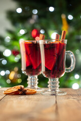 Two glass of christmas mulled wine or gluhwein with spices and orange slices on rustic table against the Christmas tree. Traditional drink on winter holiday