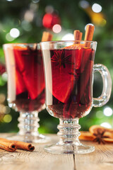 Two glass of christmas mulled wine or gluhwein with spices and orange slices on rustic table against the Christmas tree. Traditional drink on winter holiday