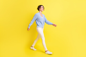 Fototapeta na wymiar Photo of lovely girl walk look empty space wear blue cardigan trousers footwear isolated yellow color background