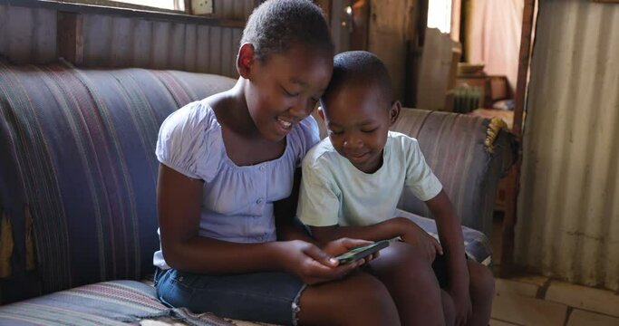 Poverty.Inequality.Close-up of young Black African boy and girl laughing using a smartphone in their shack