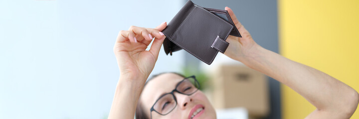 Young woman with glasses looking empty wallet at home