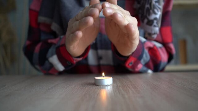 Close-up of male hands warming up near a burning candle which stands on the table. concept of problems with heating, cold at home in winter.