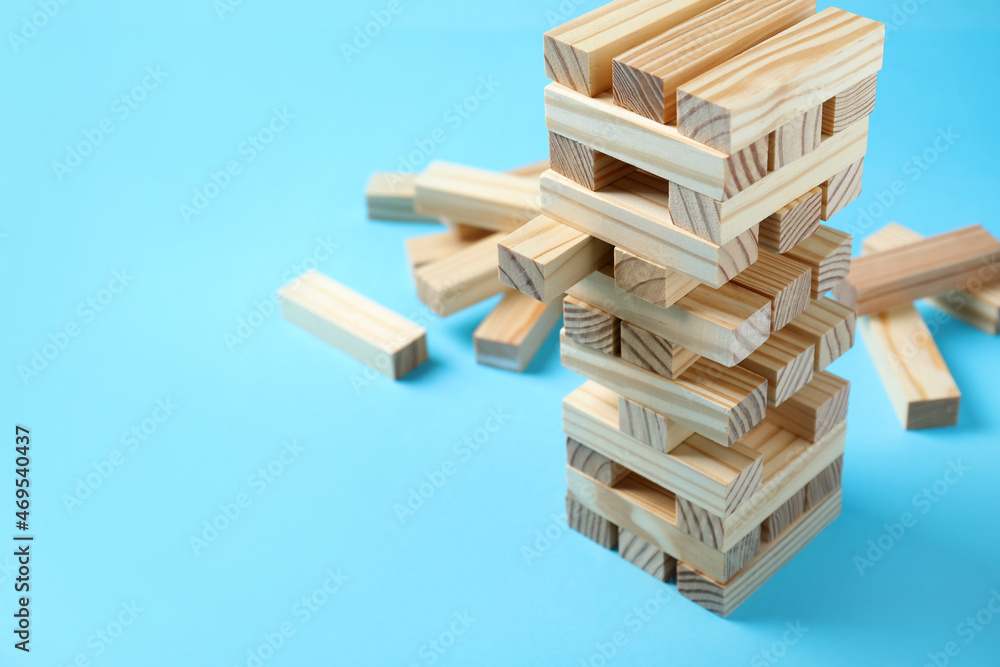 Wall mural Jenga tower and wooden blocks on light blue background, space for text