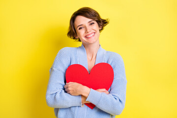 Photo of young cheerful girl happy positive smile hug big red heart feeling romantic isolated over yellow color background