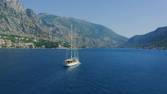 Sailing yacht in the water against the backdrop of the mountains, white sailingboat in the Bay of Kotor in Montenegro. Aerial drone view 4K.