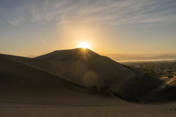 Fototapeta na wymiar amanecer con sol brillante en cuidad con dunas de arena