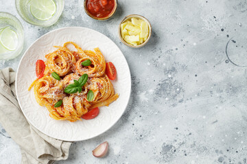 Tasty appetizing classic italian tagliatelle pasta with tomato sauce, cheese parmesan and basil on plate on light table. View from above, horizontal. Top view with copy space