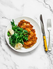Garlicky bread crumbs crispy turkey chop and fresh lemon arugula salad on a light background, top view