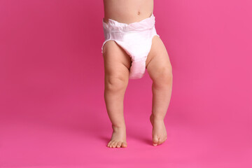 Cute baby in dry soft diaper standing on pink background, closeup