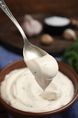 Spoon with creamy dill sauce over bowl, closeup