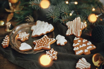 Christmas gingerbread cookies, fir branches, warm lights on napkin and rustic wooden table. Moody atmospheric image. Winter hygge. Happy Holidays and Seasons greeting