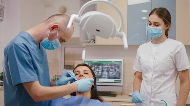 Young dentist man have a oral examination of woman patient in a modern luminous dental clinic the female assistant looking careful how dentist are working