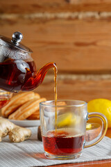 Strong saturated tea is poured into a cup from a glass teapot next to lemon and ginger.