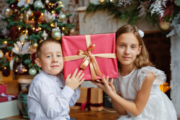 Fototapeta na wymiar The children leaned their heads against the gift. A girl and a boy with gifts under the Christmas tree. Brother and sister are happy with New Year's gifts.