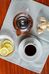 Teapot and a cup of strong aromatic tea on the table next to ginger and lemon top view.