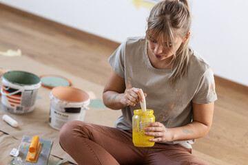 Young female preparing and mixiig paint to decorate walls in her new home.	
