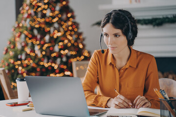Focused European lady support consultant in headset with mic working at christmas time from home