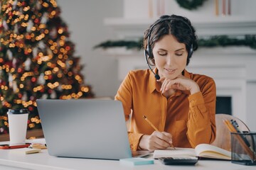 European female call center oparator in headset with mic working during winter holidays