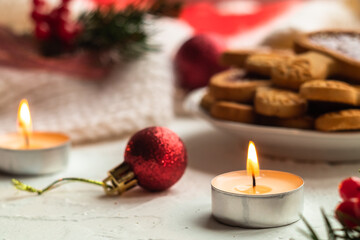 Christmas composition with a small candle close up on a light background among cookies and spruce branches.