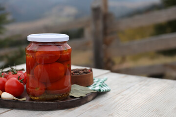 Jar of delicious pickled tomatoes and ingredients on wooden table outdoors, space for text