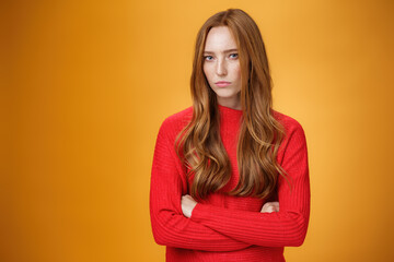 Suspicious intense and defensive ginger girl standing in passive-aggressive pose pouting and frowning looking with disbelief and disdain at camera, offended against orange background - obrazy, fototapety, plakaty
