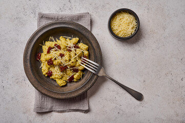 Traditional Mediterranean and Alpine potato gnocchi with parmesan and dried tomatoes in ceramic plate, with fork on napkin. Top view