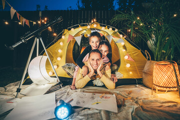 Father with cute children draws treasure map near decorated play tent with fairy lights and...