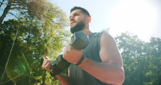 Sporty man lifting weights with both hands in a public park, Biceps training