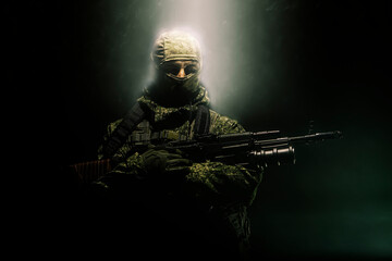Fototapeta premium A member of a special purpose unit. Russian special forces soldiers with submachine gun in clouds of smoke on a black background with colored illumination.