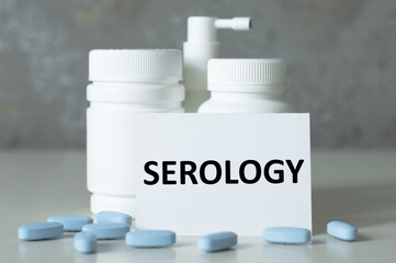 a card with text SEROLOGY on the table next to medicine jars, pills, medical concept