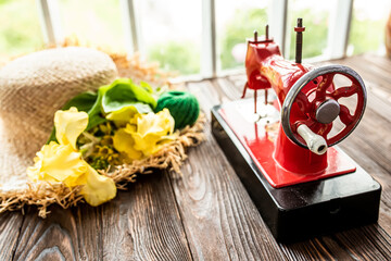 Vintage children's sewing machine on a wooden table near the window. Children's Soviet sewing machine toy in the tailor s workshop near a straw hat with fresh flowers