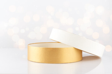 Open empty round cardboard golden gift box on a defocused lights background, front view, close-up,...