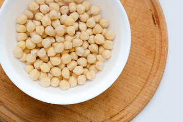 Fresh raw organic chickpeas soaked in water on a white table on a wooden tray. The benefits of legumes. Vegan nutritive proteinaceous food. Taking care of your health. Empty space. 